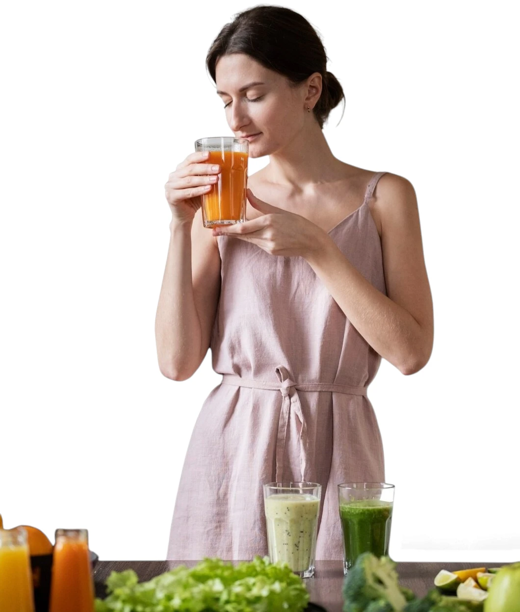 Woman drinking a glass of fresh carrot juice beside green smoothies, lettuce and broccoli