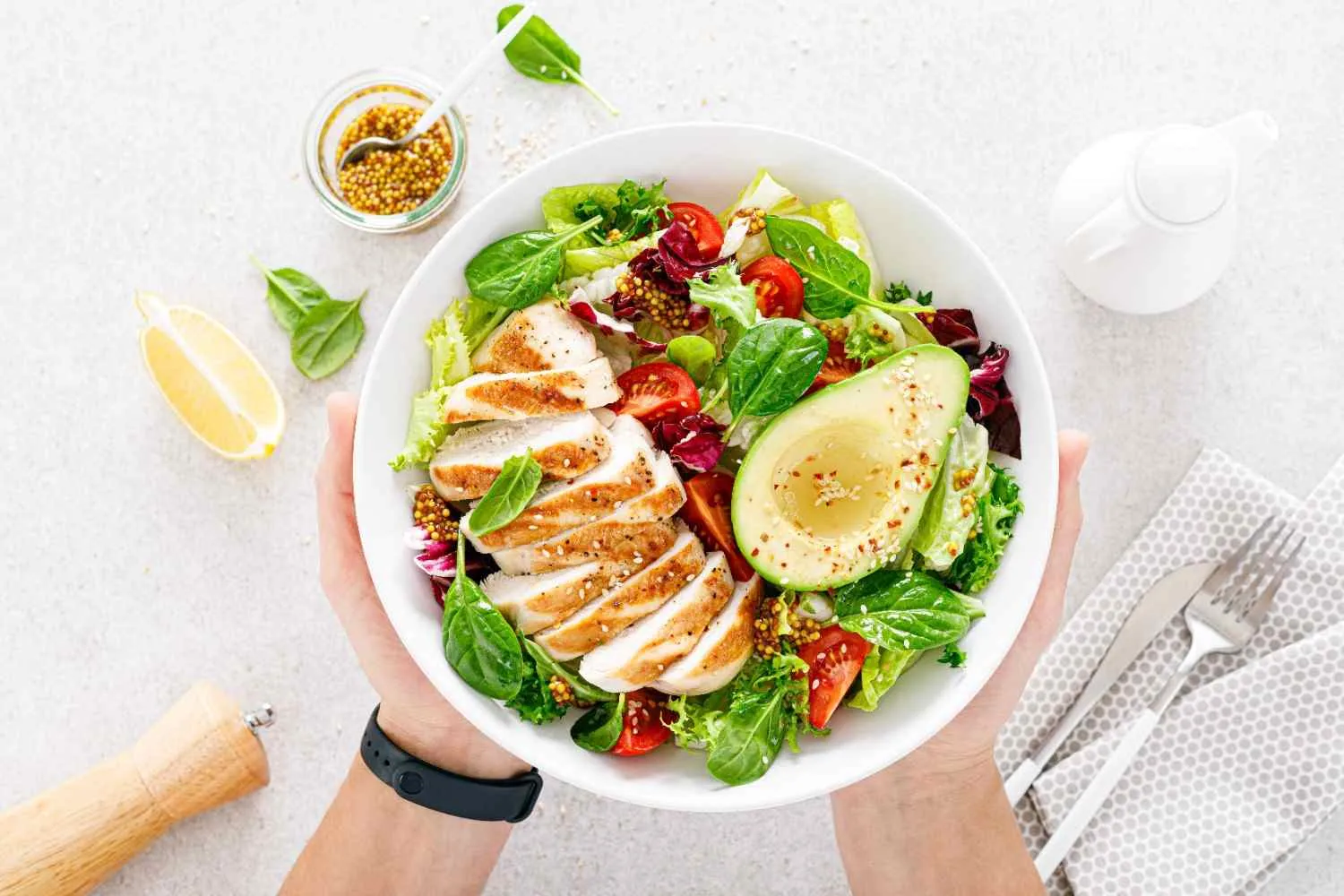 Bowl of salad with sliced chicken, avocado, spinach and tomatoes held in two hands